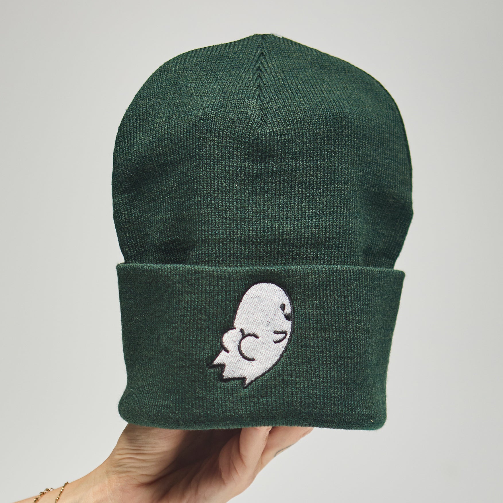 Green beanie with a white embroidered ghost with a butt design held by a hand on a neutral background