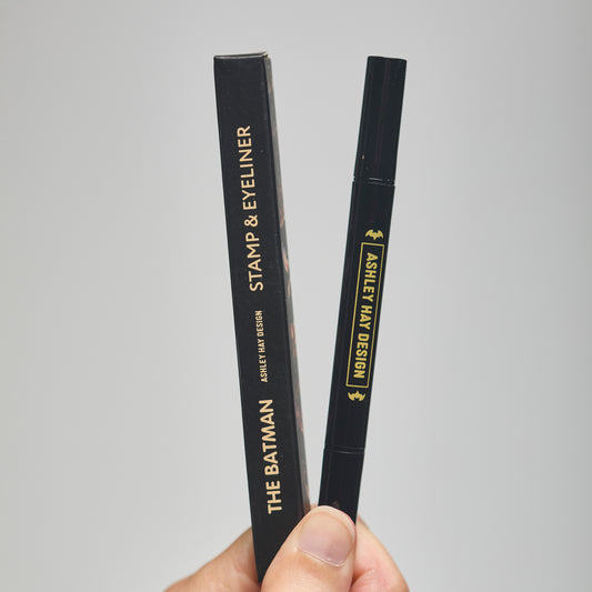 Hand holding a black makeup stamp and eyeliner package with visible branding against a neutral background