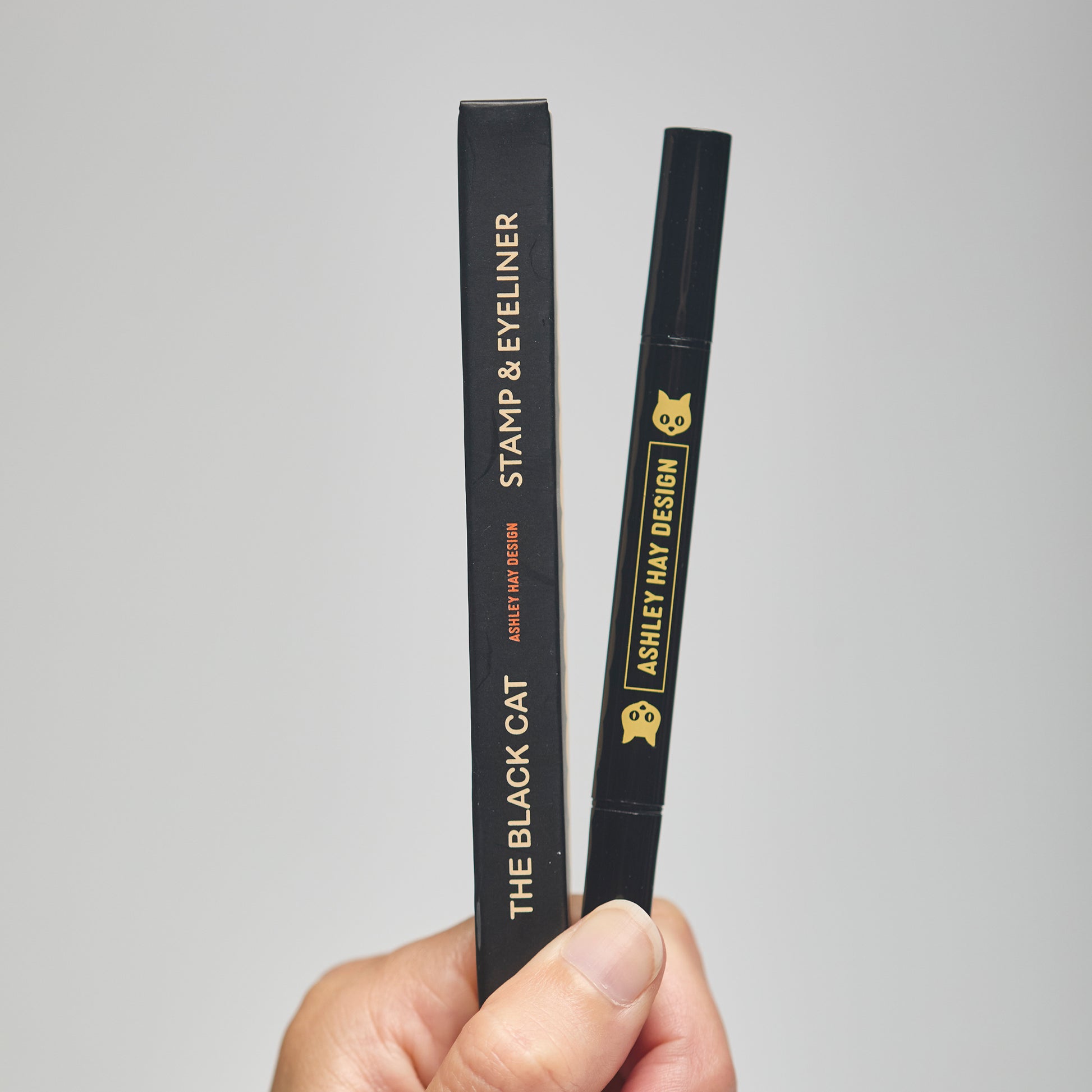 Hand holding a black makeup stamp and eyeliner package with visible branding against a neutral background