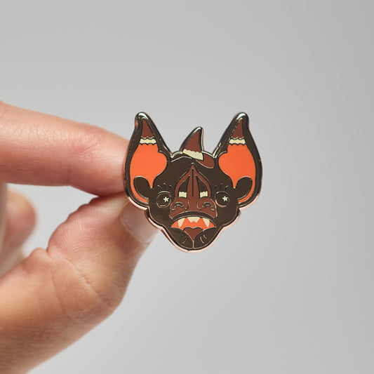 Enamel pin of a chestnut short-tailed bat held by a hand against a neutral background