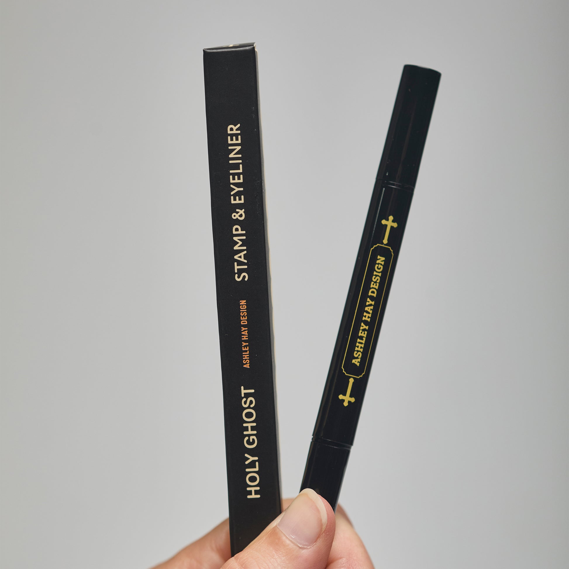 Hand holding a black makeup stamp and eyeliner package with visible branding against a neutral background