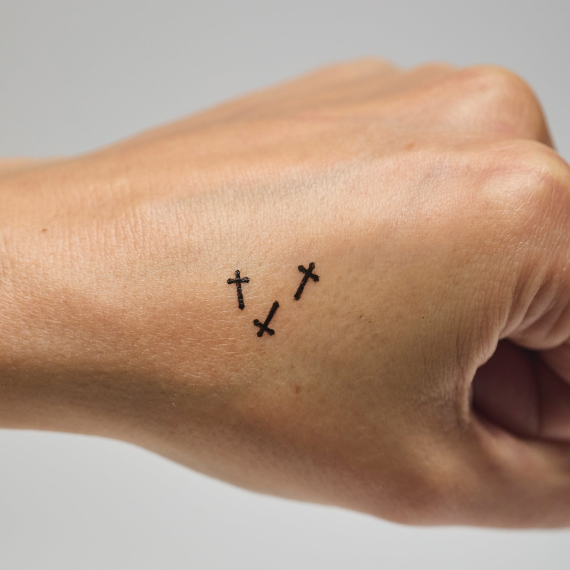 Three black cross makeup stamps on a person's hand against a neutral background