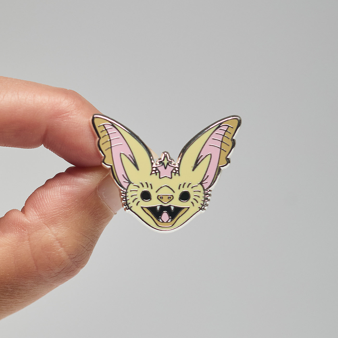 Enamel pin of a desert long-eared bat held by a hand against a neutral background