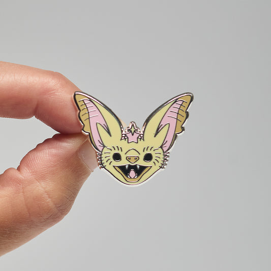 Enamel pin of a desert long-eared bat held by a hand against a neutral background