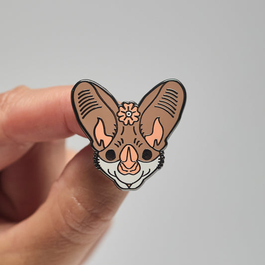 Enamel pin of a ghost bat held by a hand against a neutral background