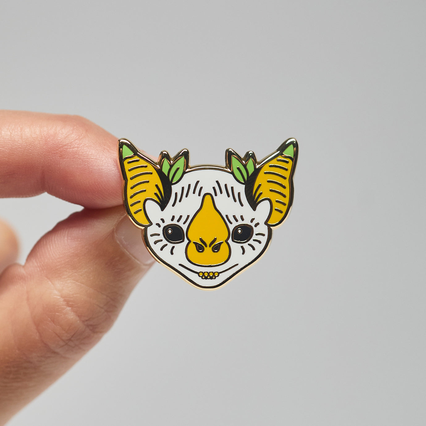 Enamel pin of a Honduran white bat held by a hand against a neutral background