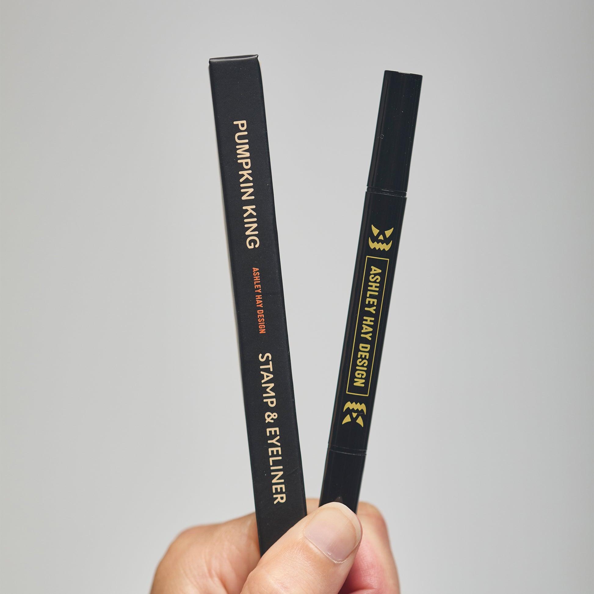 Hand holding a black makeup stamp and eyeliner package with visible branding against a neutral background