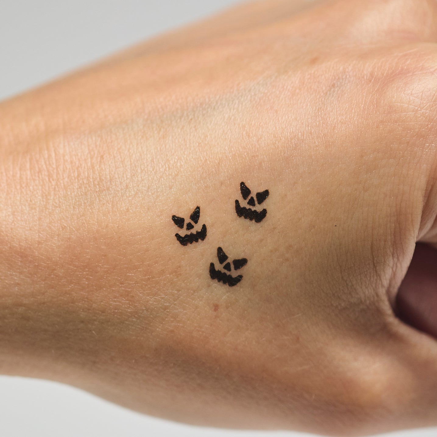 Three black jack-o-lantern face makeup stamps on a person's hand against a neutral background