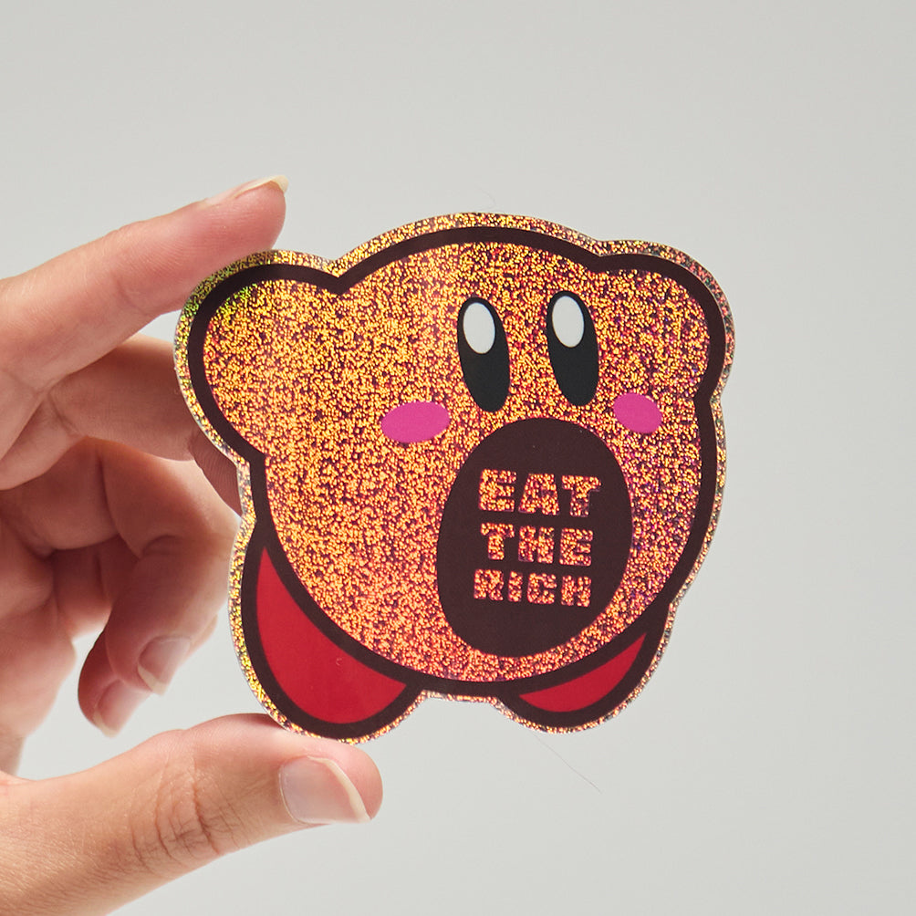 Sticker of Kirby that says 'Eat the Rich' text held by a hand on a neutral background