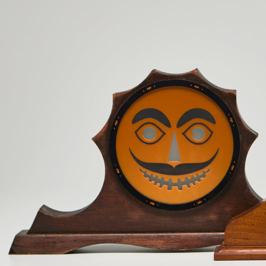 Decorative Halloween piece with a jack-o'-lantern face on a wooden stand against a neutral background