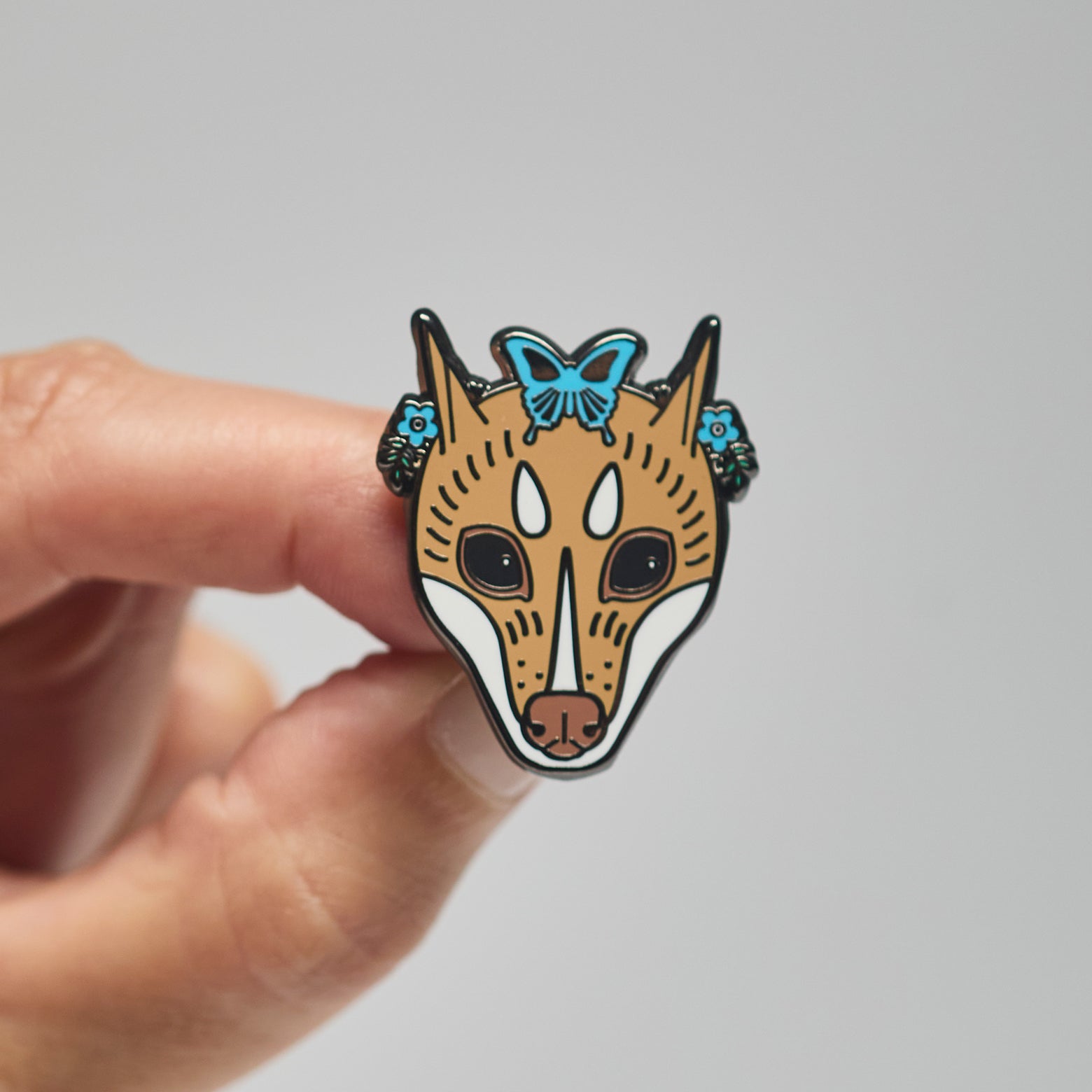 Enamel pin of a mindoro stripe-faced bat held by a hand against a neutral background