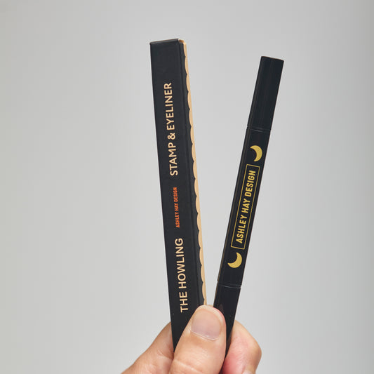 Hand holding a black makeup stamp and eyeliner package with visible branding against a neutral background