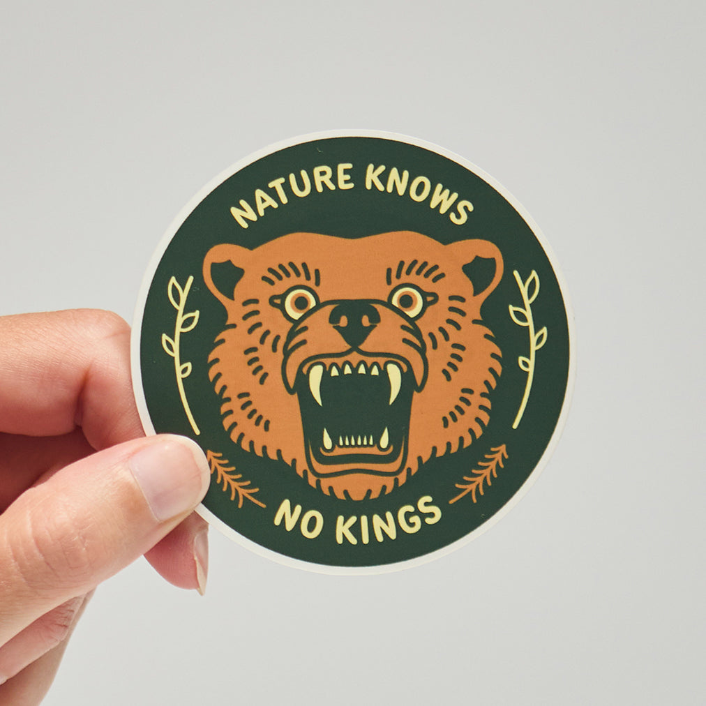 Sticker with bear illustration and text 'Nature Knows No Kings' held by a hand on a neutral background