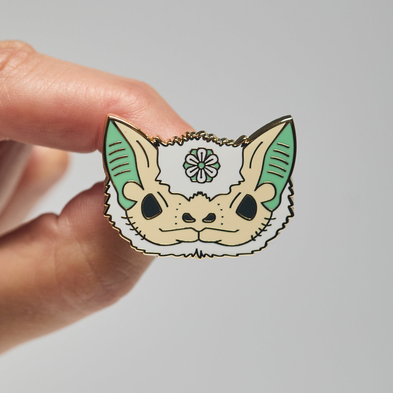 Enamel pin of a Northern ghost bat held by a hand against a neutral background