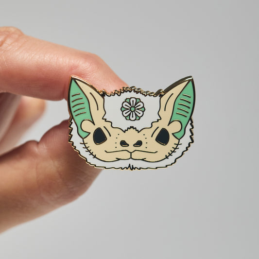 Enamel pin of a Northern ghost bat held by a hand against a neutral background