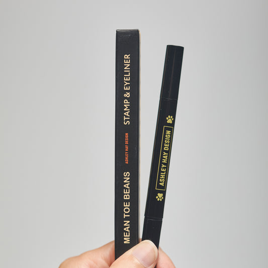 Hand holding a black makeup stamp and eyeliner package with visible branding against a neutral background