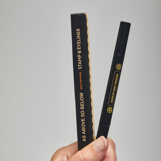 Hand holding a black stamp and eyeliner  packaging with visible branding against a gray background