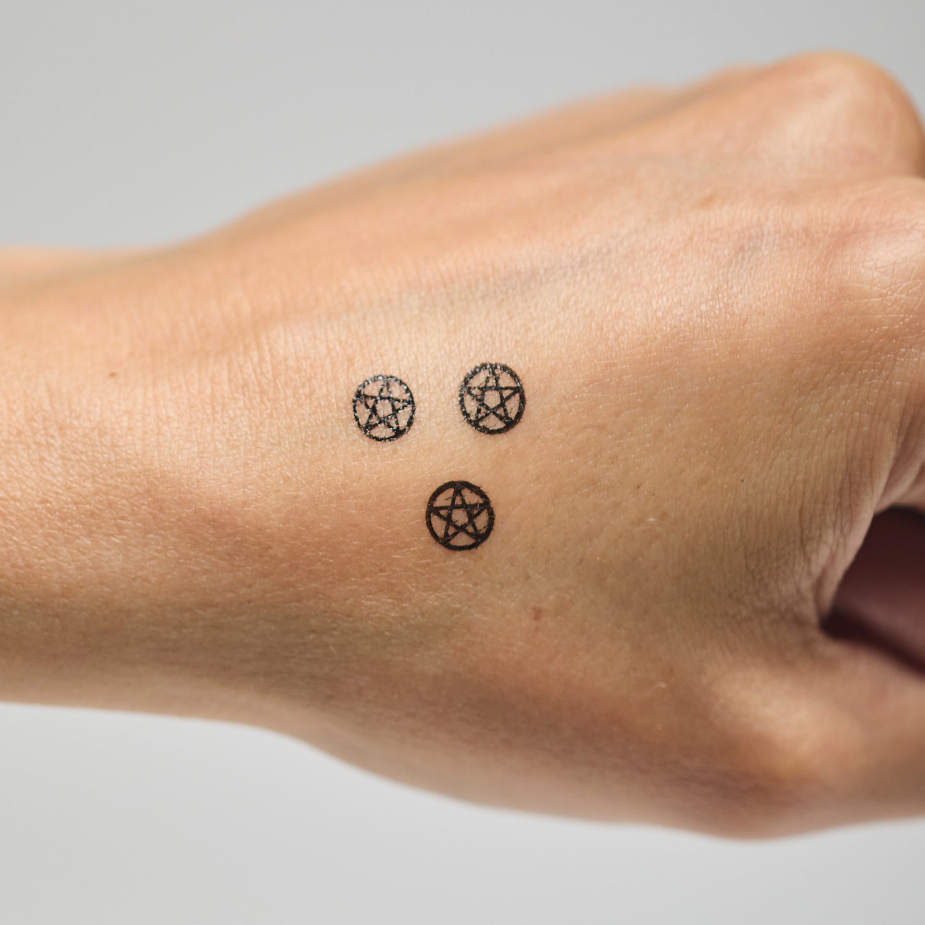 Three black pentacle makeup stamps on a person's hand against a neutral background
