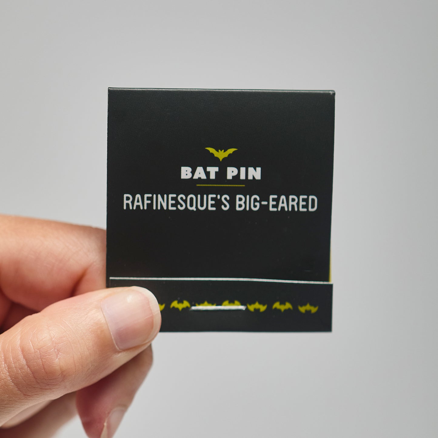 A black match book with 'Bat Pin Rafinesque's Big-eared' text held by a hand against a neutral background