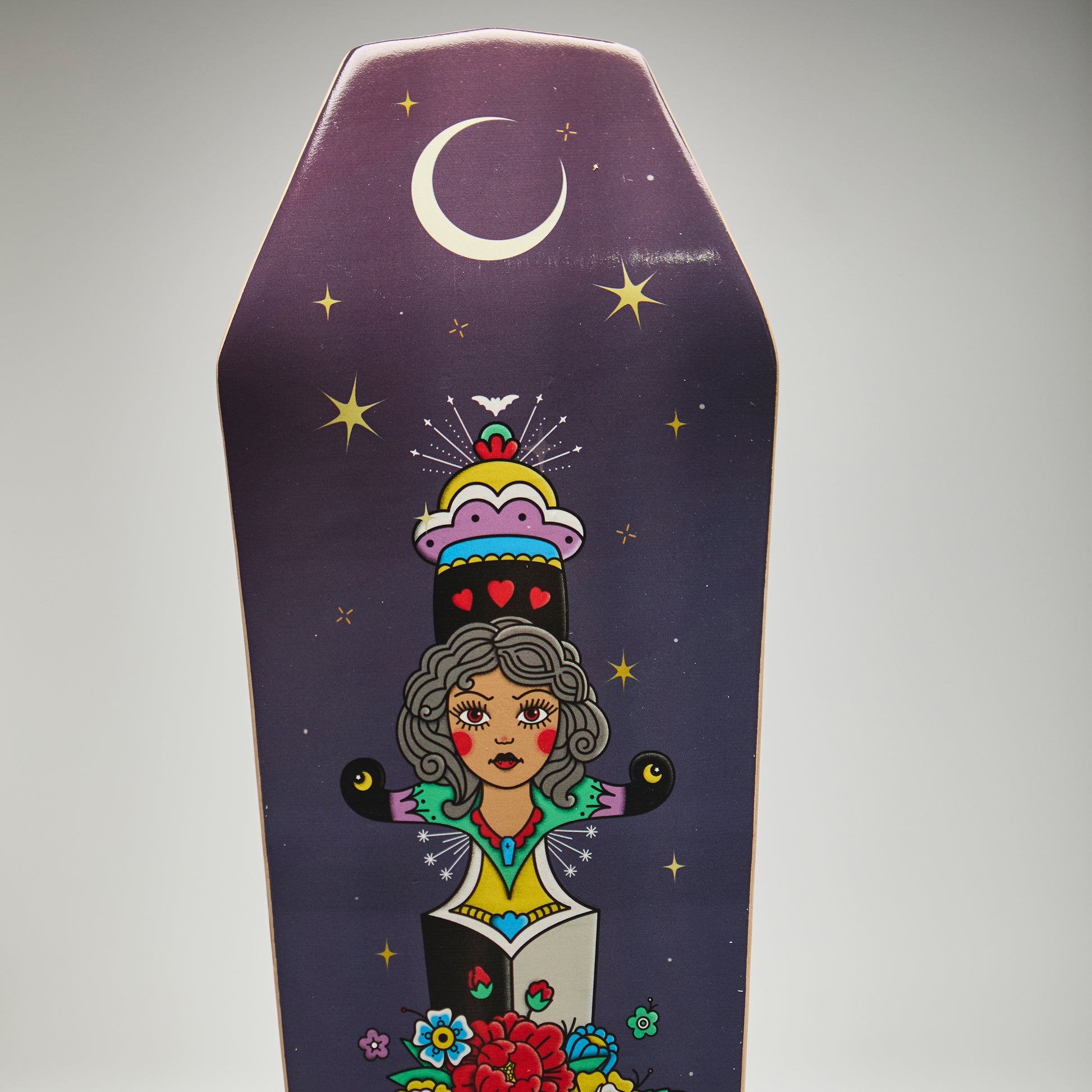 Decorative coffin-shaped skateboard deck with colorful illustration of a woman and celestial elements on a purple background.