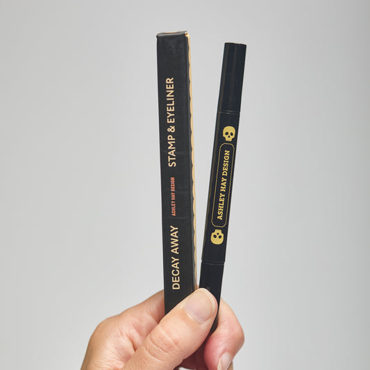 Hand holding a black makeup stamp and eyeliner package with visible branding against a neutral background