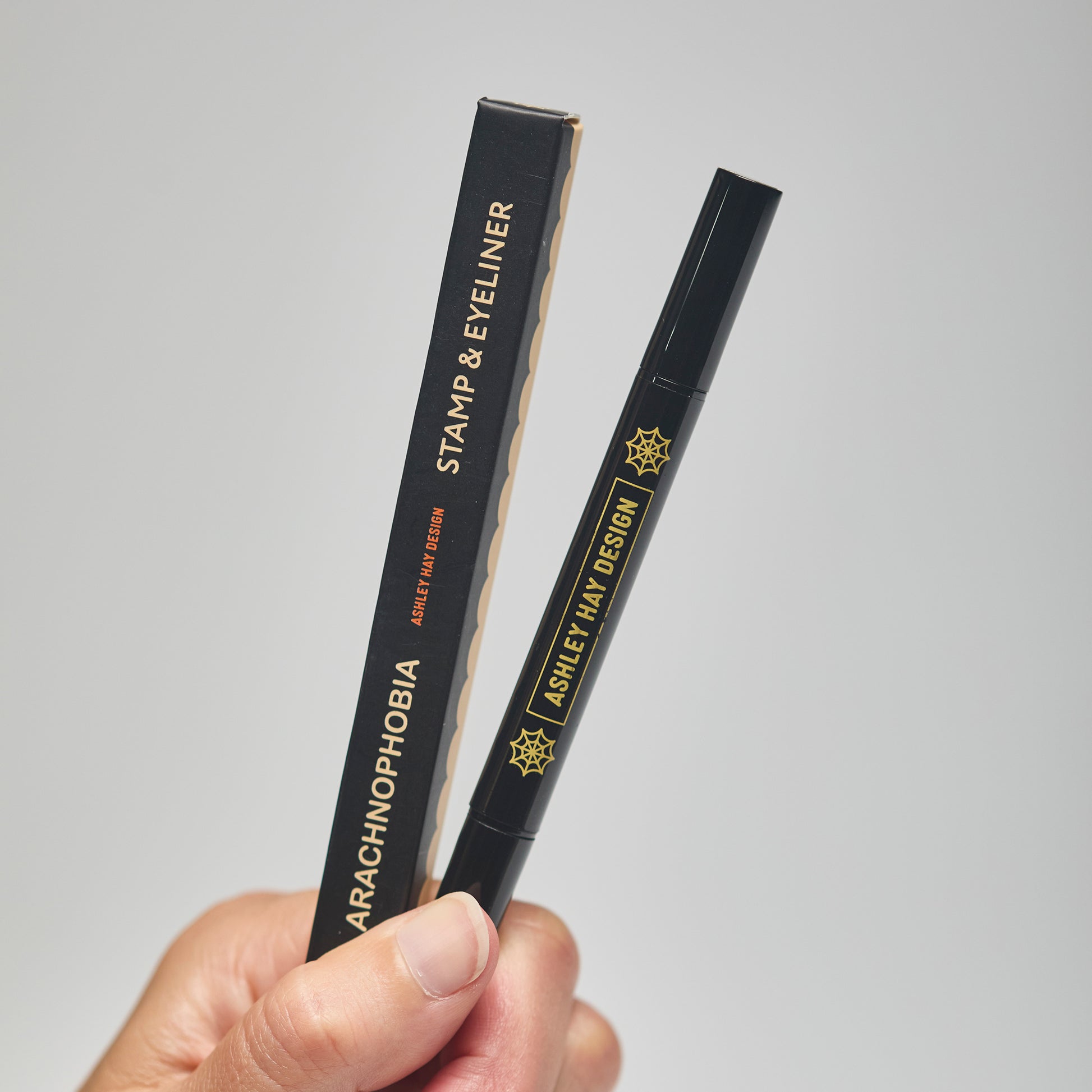 Hand holding a black makeup stamp and eyeliner package with visible branding against a neutral background