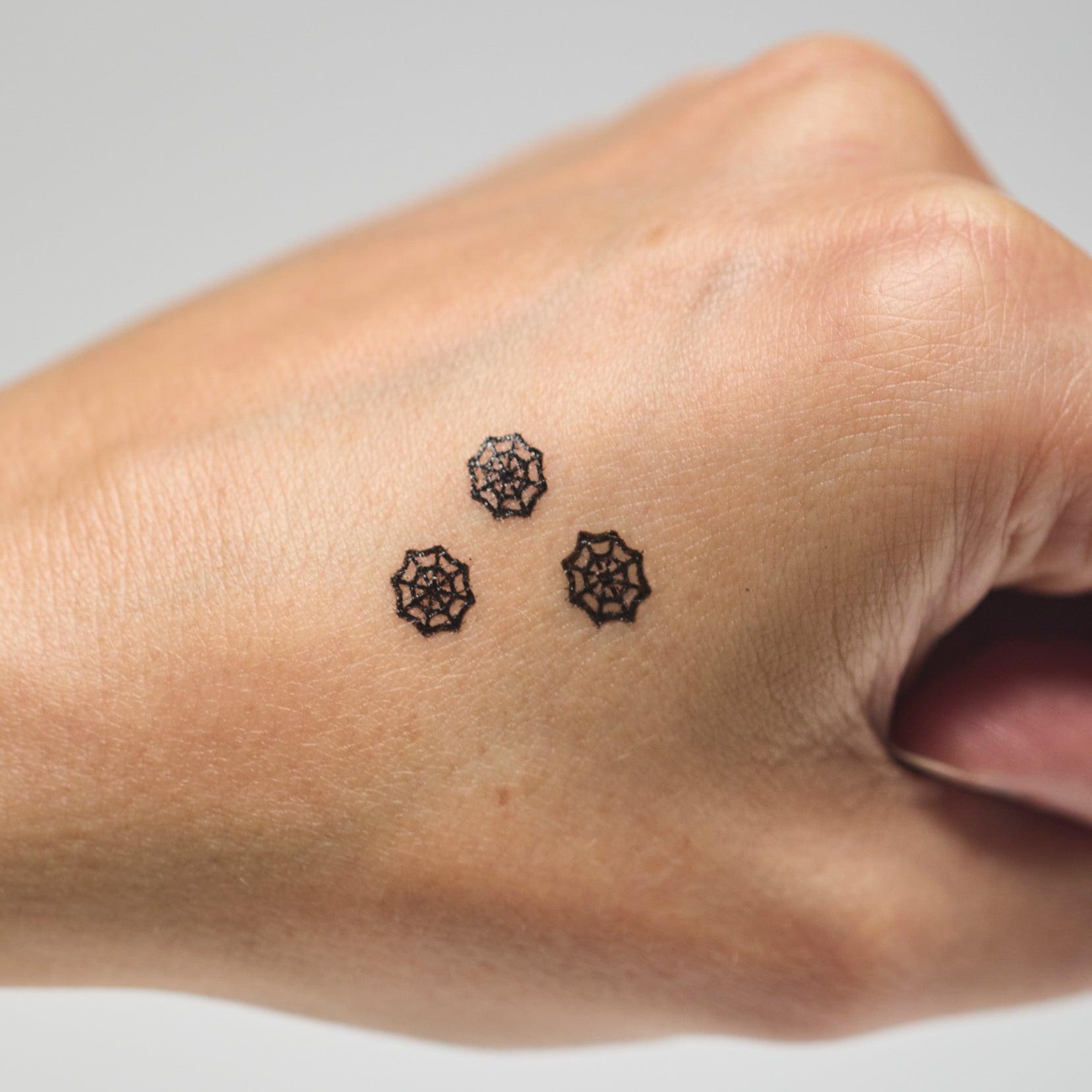 Three black spider web makeup stamps on a person's hand against a neutral background