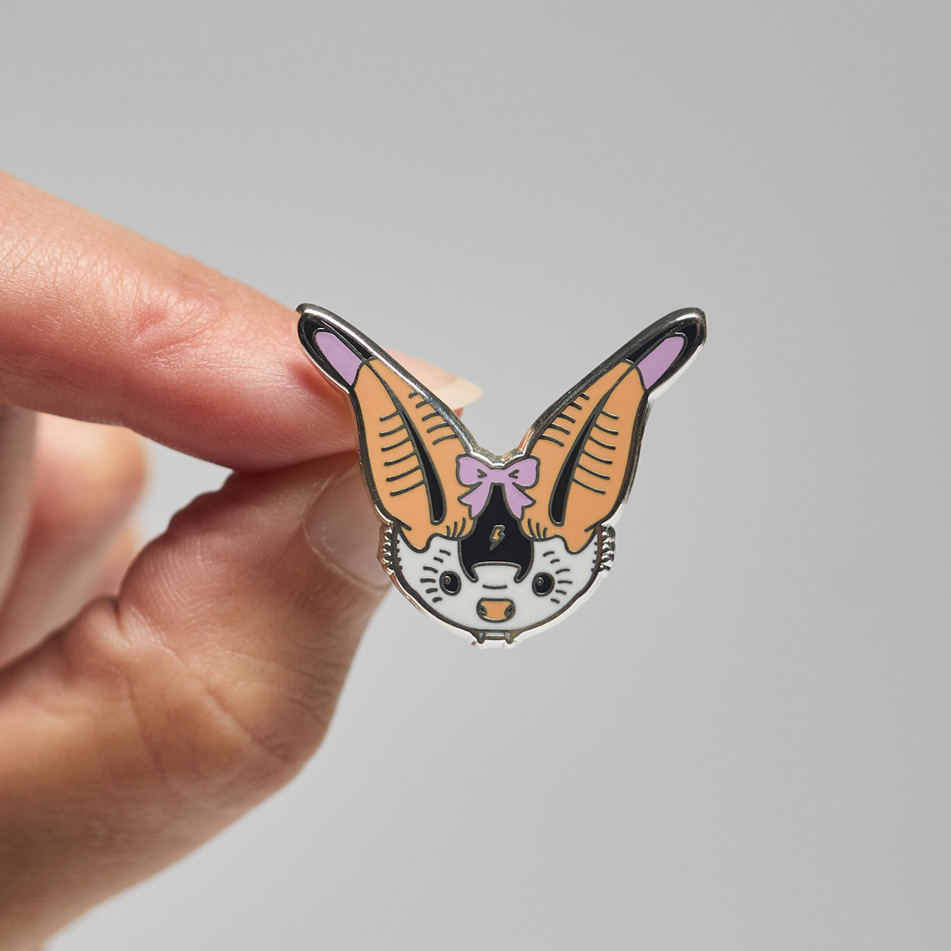Enamel pin of a spotted bat held by a hand against a neutral background
