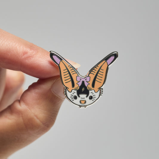 Enamel pin of a spotted bat held by a hand against a neutral background