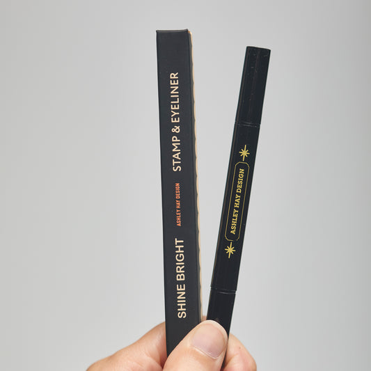 Hand holding a black makeup stamp and eyeliner package with visible branding against a neutral background