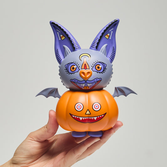 Halloween-themed toy with big ears and pumpkin body held by a hand against a gray background