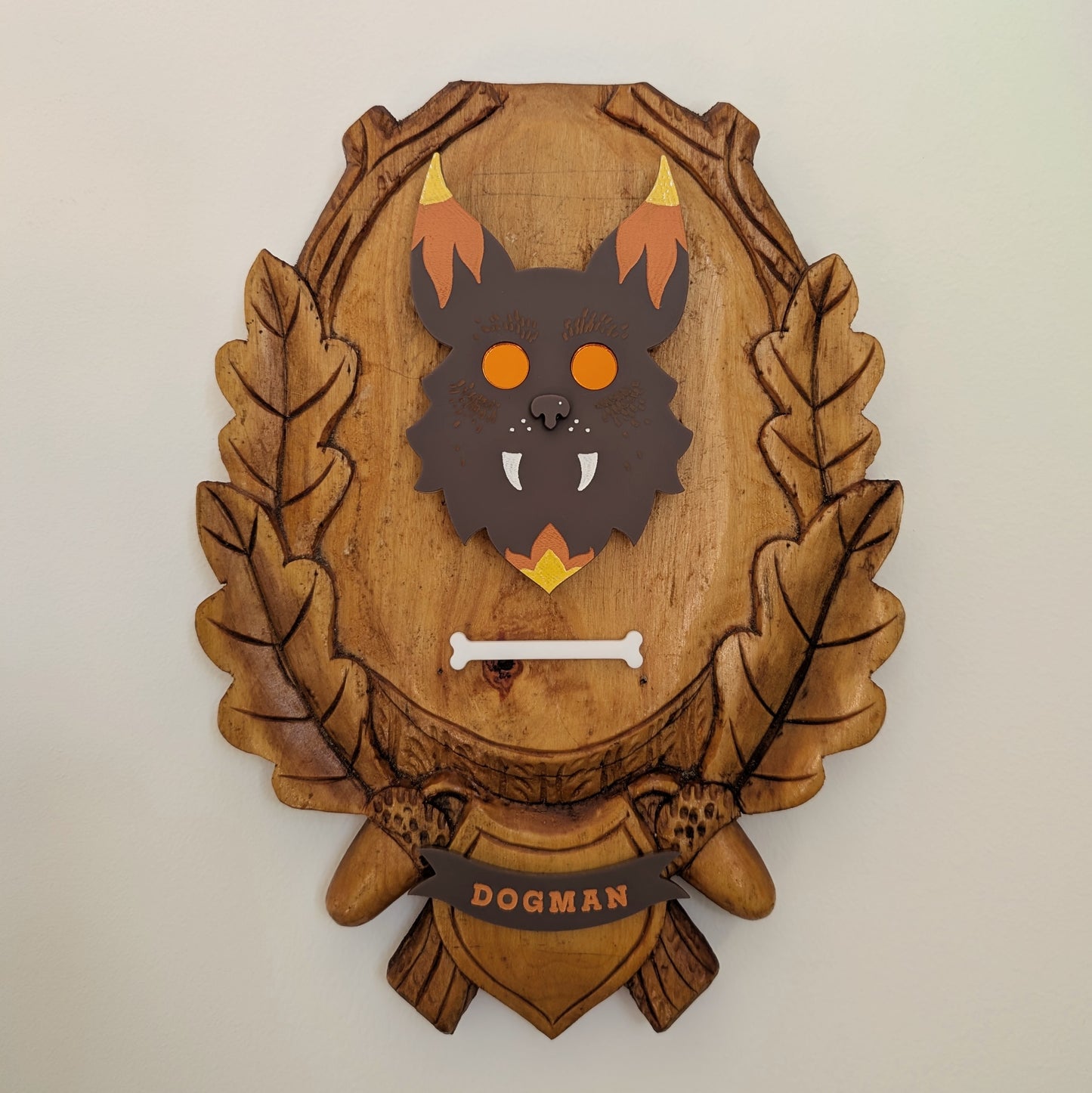 An acrylic Dogman head mounted on a wooden plaque hangs on a white wall.