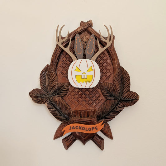Vintage wooden wall piece with jack-o'-lantern/rabbit face and Jackalope scoll hanging on a beige background.
