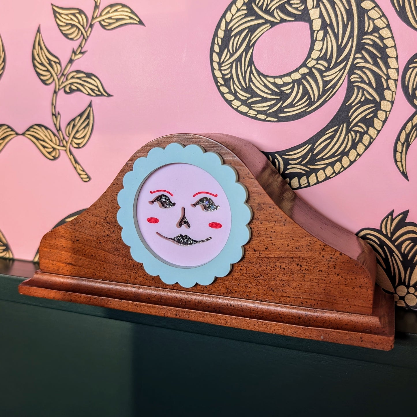 A vintage wood clock frame repurposed with a pink jack-o-lantern face. The face is framed by a pastel scallop ring.