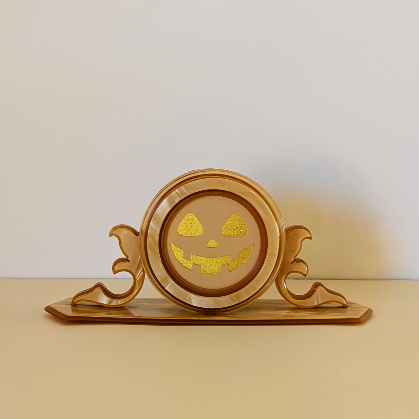 A vintage plastic clock frame repurposed with a yellow jack-o-lantern face.