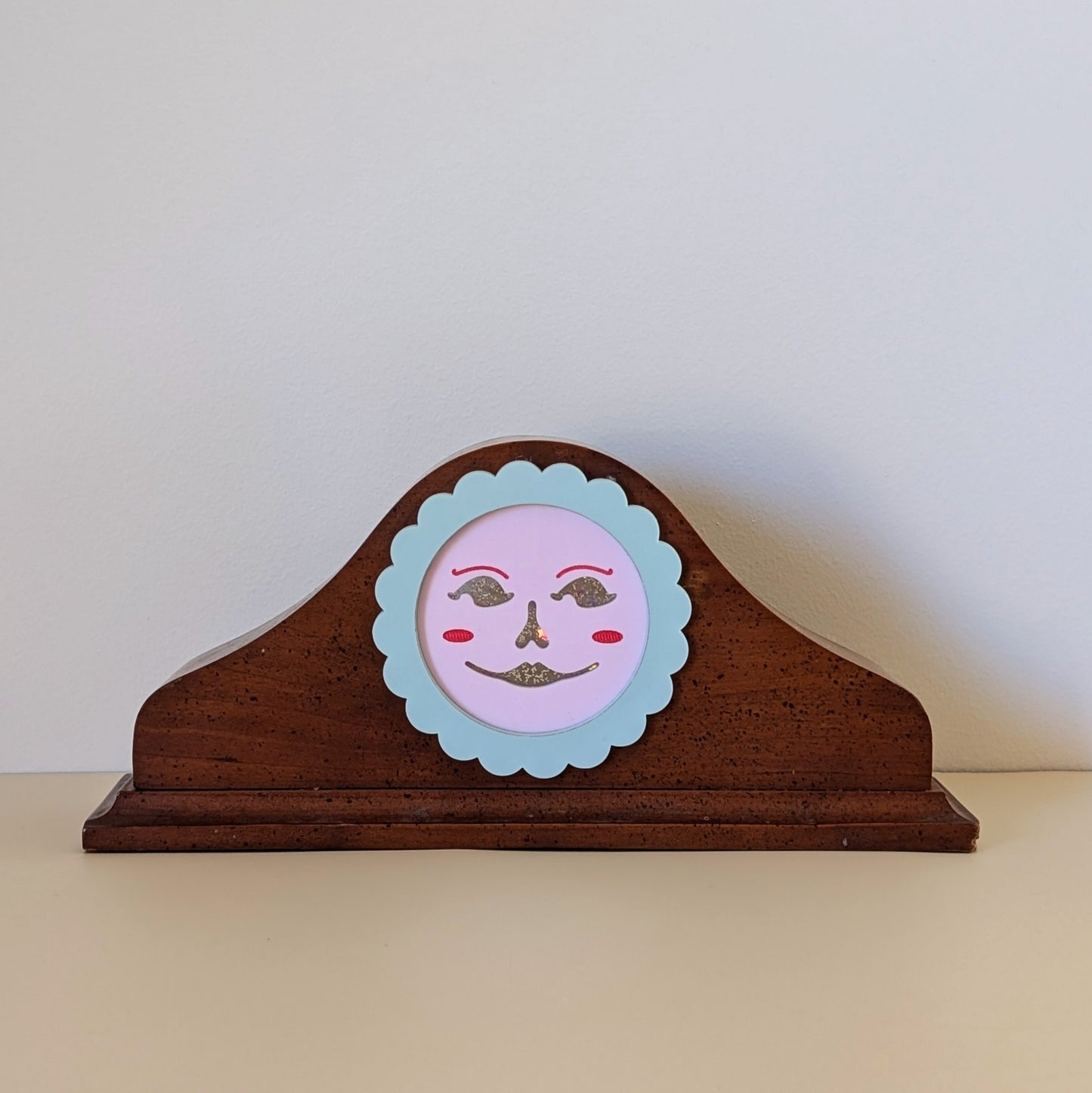 A vintage wood clock frame repurposed with a pink jack-o-lantern face. The face is framed by a pastel scallop ring.