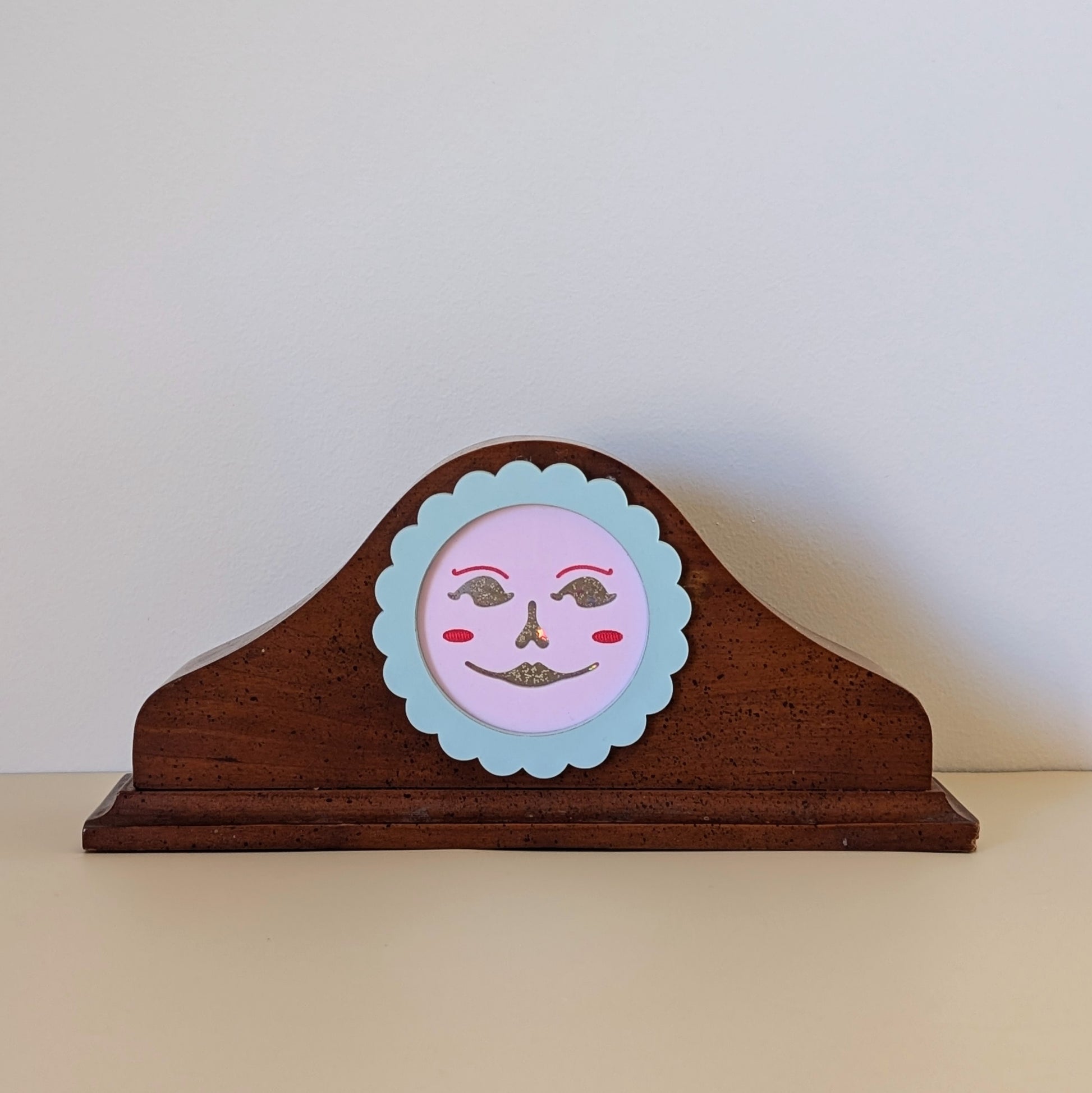 A vintage wood clock frame repurposed with a pink jack-o-lantern face. The face is framed by a pastel scallop ring.
