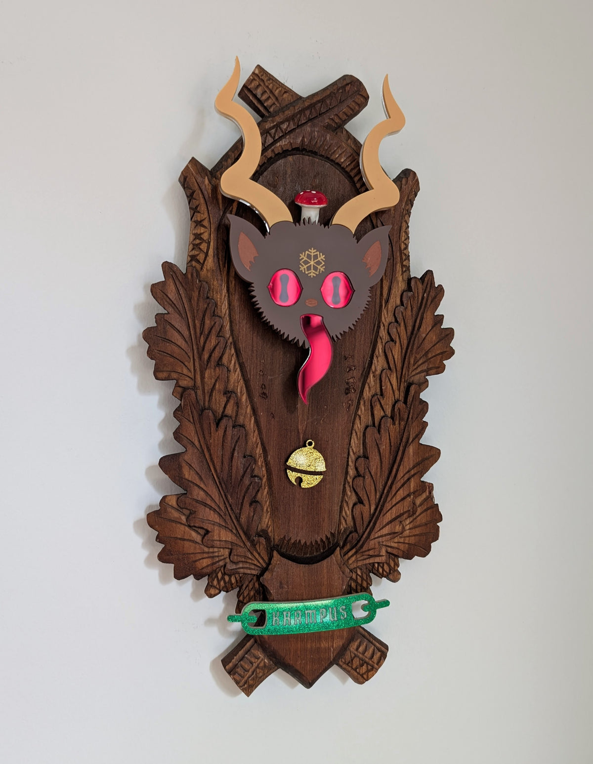 Krampus's face is mounted on a vintage wooden plaque that hangs on a white wall.
