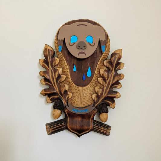 Wooden wall decoration with a squonk face and blue tears hanging on a beige wall.