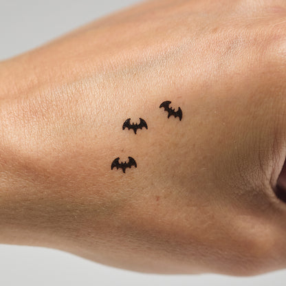 Three black bat makeup stamps on a person's hand against a neutral background