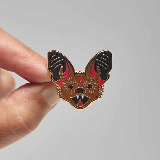 Enamel pin of a little brown bat held by a hand against a neutral background