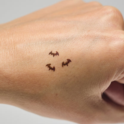 Three brown bat makeup stamps on a person's hand against a neutral background