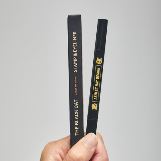 Hand holding a black makeup stamp and eyeliner package with visible branding against a neutral background