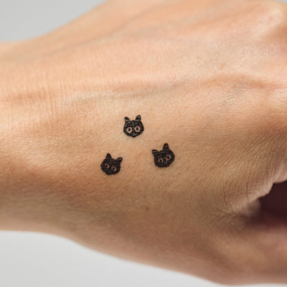Three black cat makeup stamps on a person's hand against a neutral background