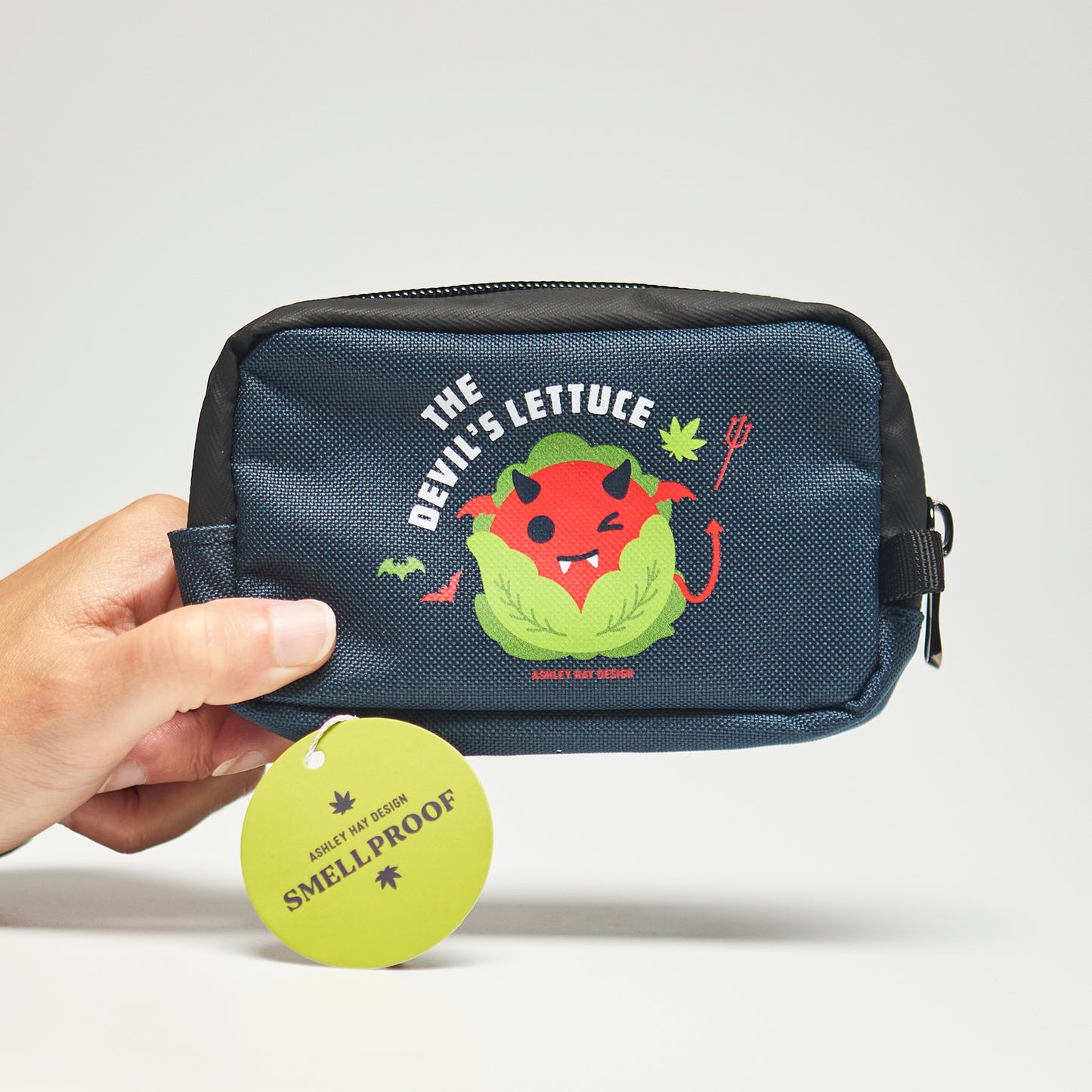 Navy smellproof bag with a cute lettuce character labeled 'The Devil's Lettuce' held by a hand on a neutral background.