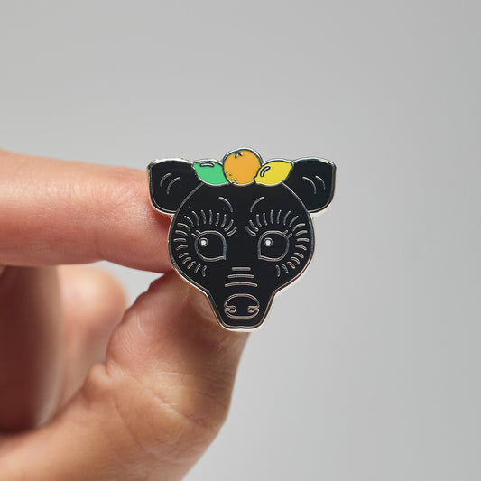 Enamel pin of a black fruit bat held by a hand against a neutral background
