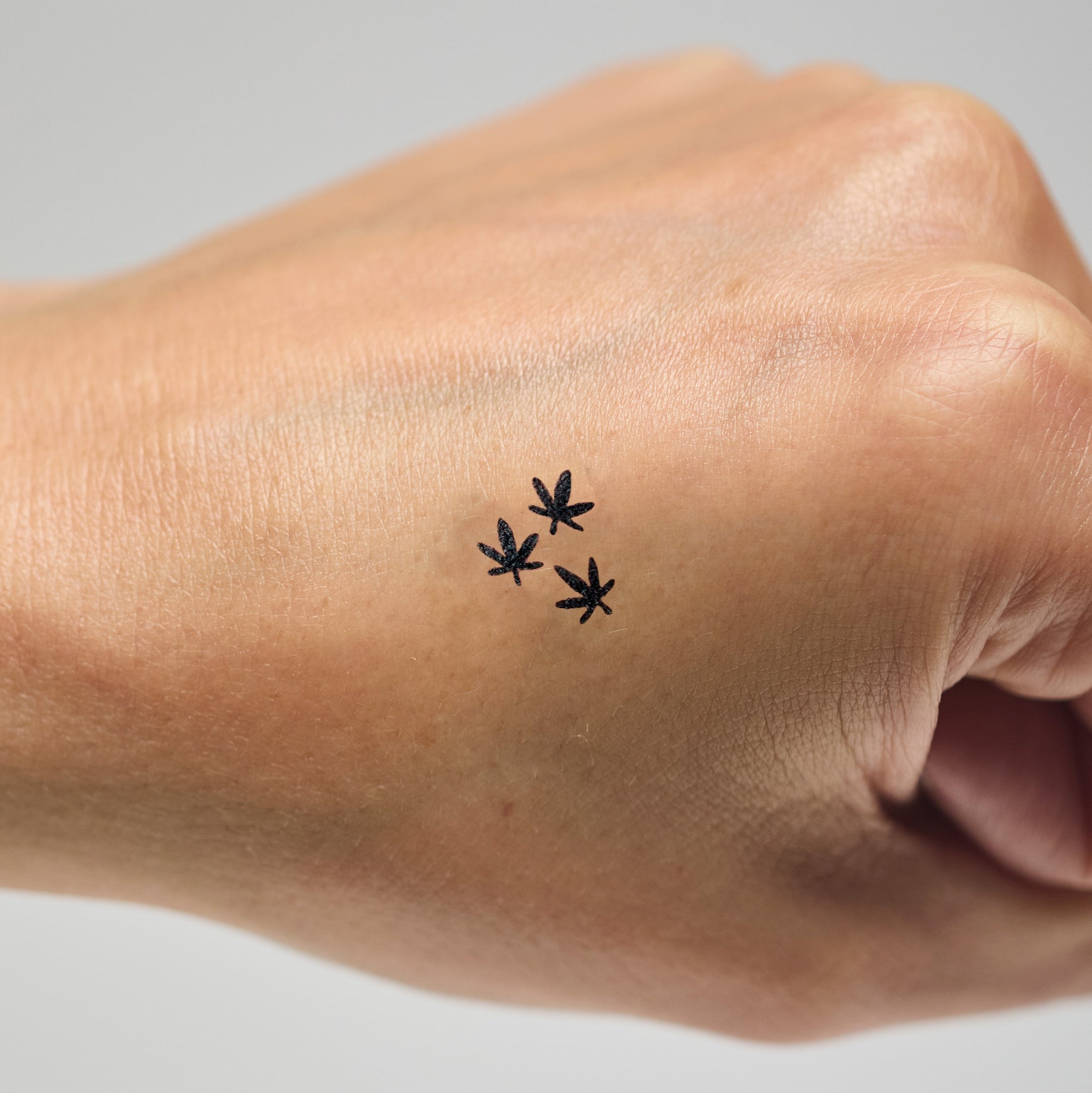 Three small black stamps of leaves on a person's hand against a neutral background