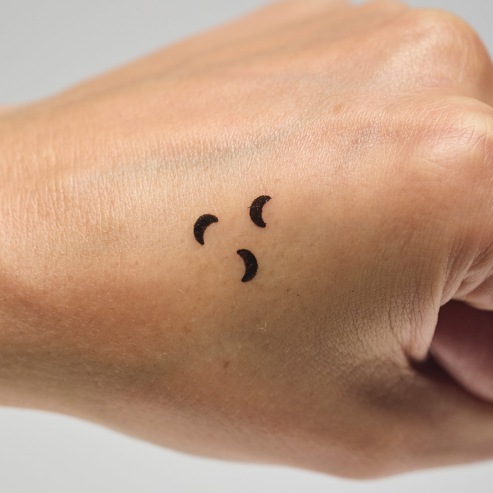Three black moon makeup stamps on a person's hand against a neutral background
