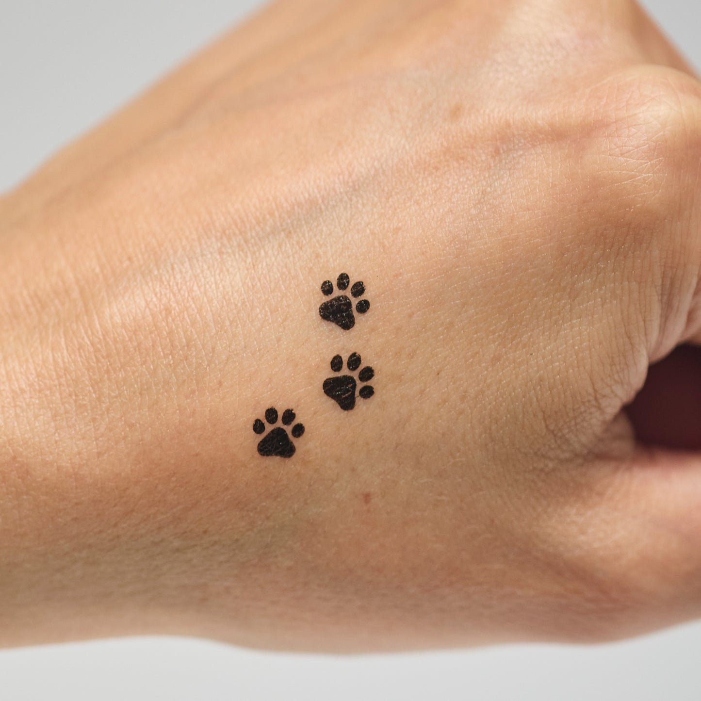 Three black paw print makeup stamps on a person's hand against a neutral background