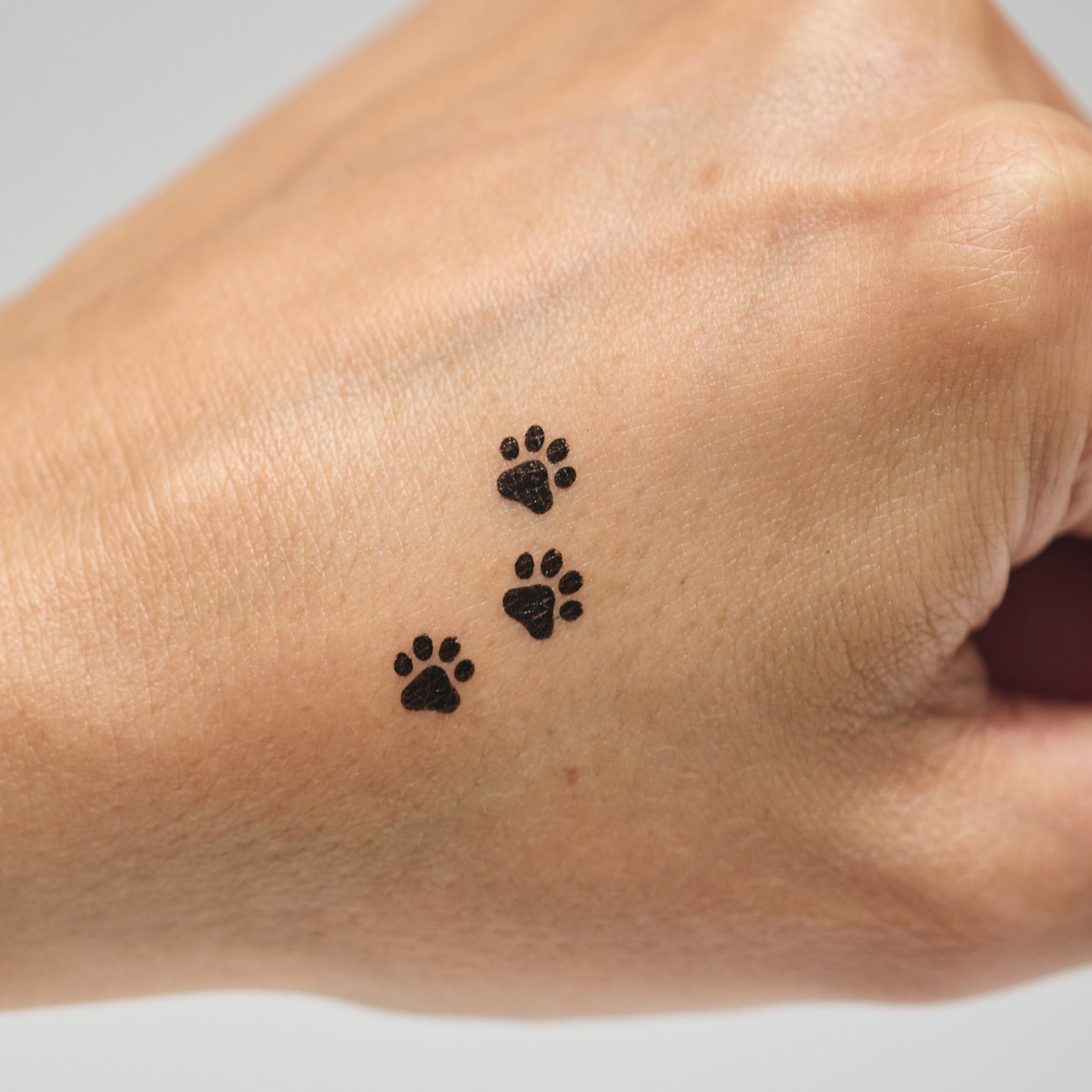 Three black paw print makeup stamps on a person's hand against a neutral background